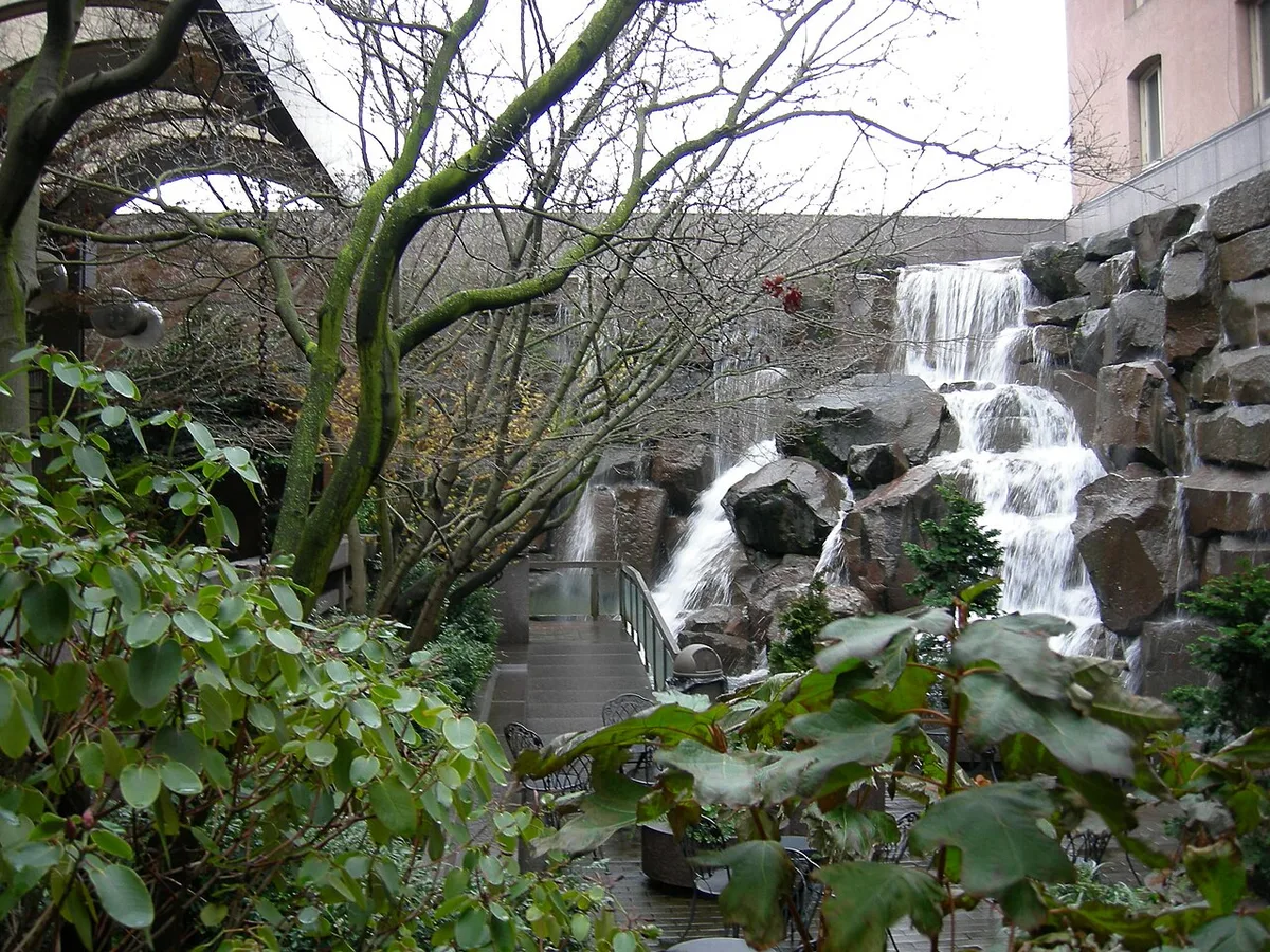 Een aangelegde waterval stort over gestapelde rotsblokken omlaag in een beplante binnentuin.